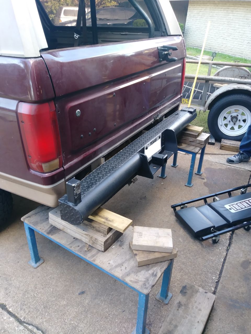 Maroon Ford Bronco with custom black diamond plate bumper on wooden blocks.