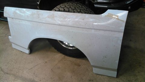 1992 Ford Bronco - A white, unpainted rear fender assembly for a 1992 Ford Bronco is shown in a workshop setting. The part is resting on a concrete floor, wit…