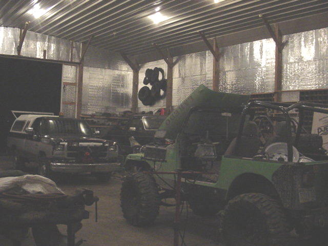 Two off-road vehicles inside a garage, one green, one dark colored with a cap