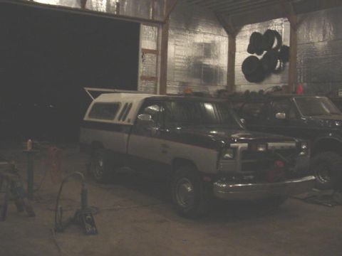 1992 Ford Bronco - Two pickup trucks are parked inside a garage, one with a camper shell is in the foreground.