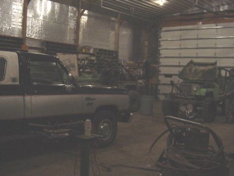 1992 Ford Bronco - Two vehicles, a pickup truck and a jeep, are parked inside a garage with large roll-up doors.