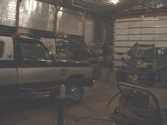 pickup truck with camper shell parked next to a green jeep with hood up in a garage