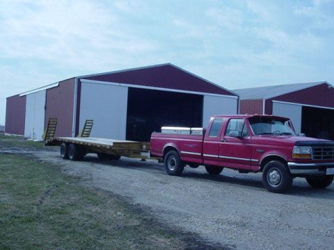 1992 Ford Bronco - A red Ford F-250 pickup truck from the mid-1990s is seen towing a flatbed trailer in front of a large barn.
