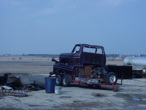1992 Ford Bronco - A truck cab sits on a trailer, with a large tank visible in the background, under a cloudy sky.