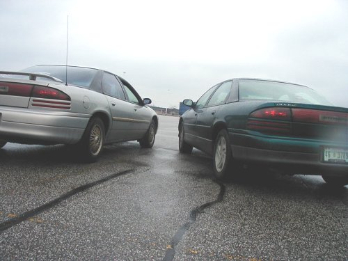 Two green and silver Dodge Intrepids on a wet asphalt surface, rear view