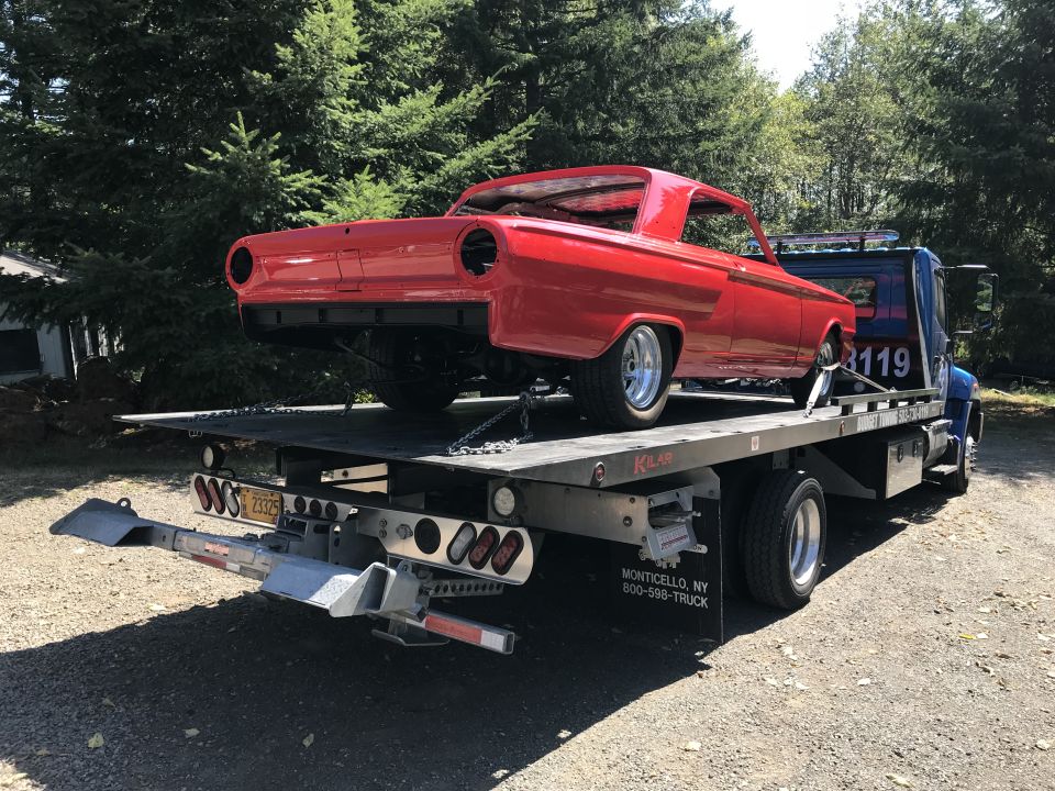 Red classic car body on a flatbed tow truck.