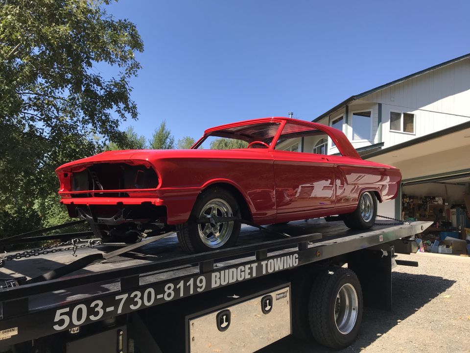 Red 1964 Ford Fairlane coupe being towed on a flatbed truck.