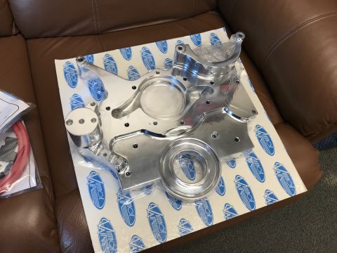 1964 Ford Fairlane - A polished aluminum engine timing cover is displayed on a white paper with blue logos. The part is placed on a brown leather couch.