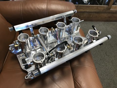 1964 Ford Fairlane - A highly polished, custom aluminum intake manifold with six throttle bodies and fuel rails is displayed on a brown leather surface. The man…