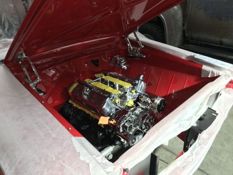 1964 Ford Fairlane - The engine bay of a red classic car is shown with a highly polished chrome engine and intake manifold. The hood is open, revealing the engi…