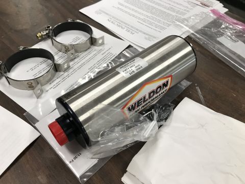 1964 Ford Fairlane - A Weldon fuel pump with associated mounting hardware and documentation are laid out on a wooden surface. The fuel pump is cylindrical and s…
