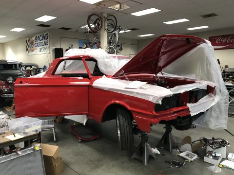 1964 Ford Fairlane - A bright red 1964 Ford Fairlane coupe is undergoing restoration in a garage. The car is on jack stands with its hood and driver's door open…