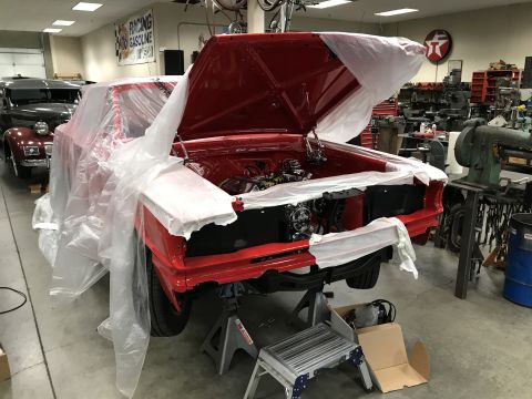 1964 Ford Fairlane - A bright red classic car, possibly a 1964 Ford Fairlane, is covered in protective plastic sheeting in a workshop. The hood is open, reveali…