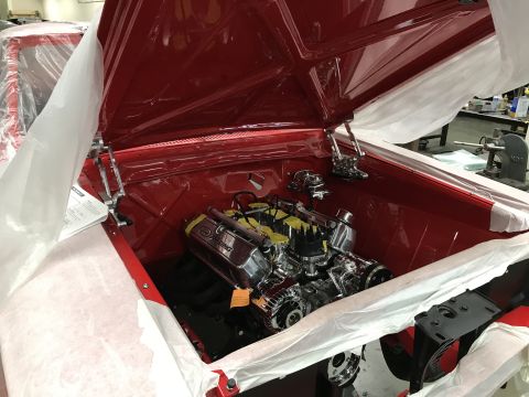 1964 Ford Fairlane - The engine bay of a red classic car is covered with protective white sheeting. A chrome engine with yellow valve covers is visible under th…