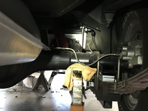1964 Ford Fairlane - The underside of a vehicle shows a rear axle assembly with a differential, leaf springs, and brake components. A large exhaust pipe runs ho…