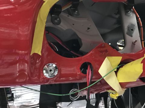 1964 Ford Fairlane - Close-up view of the red painted body panel of a vehicle, showing wiring and a chrome-plated circular fitting. Yellow masking tape is appli…