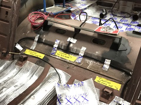 1964 Ford Fairlane - The interior floor of a classic car is being prepared for sound dampening with foil-backed material. Yellow caution labels are taped to the…