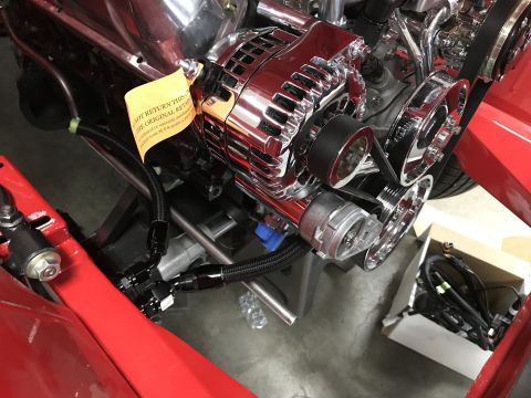 1964 Ford Fairlane - A close-up view of a chrome alternator and serpentine belt system on a V8 engine, with a yellow tag attached to the alternator. Black braid…
