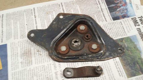 1964 Ford Fairlane - A rusty metal bracket with three bolts and a nut is shown against a background of newspaper articles. A smaller, separate metal piece with…