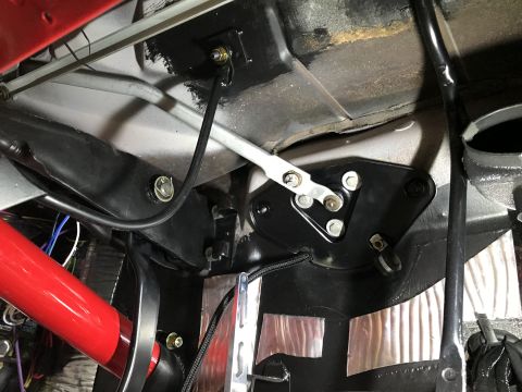 1964 Ford Fairlane - The underside of a vehicle's interior shows a black metal bracket assembly with a silver linkage arm attached. Various cables and a red cyl…