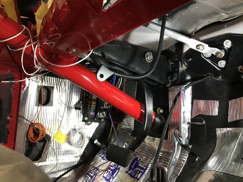 1964 Ford Fairlane - The interior of a vehicle is shown, focusing on the driver's side footwell and dashboard area. Visible components include red roll cage tub…