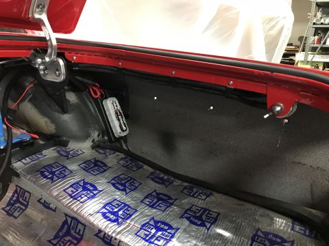 1964 Ford Fairlane - The interior of a red vehicle's trunk area shows sound deadening material on the floor and a battery tender device mounted on the side pane…