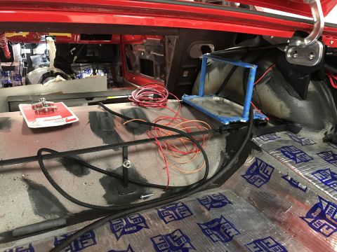 1964 Ford Fairlane - The interior of a red vehicle, likely a trunk area, is being modified with sound deadening material and wiring. A metal bracket with blue t…