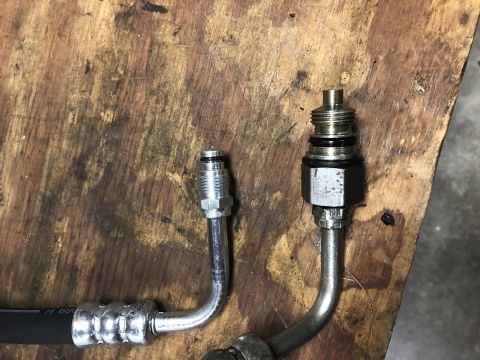 1980 Ford Bronco - Close-up of two hydraulic hoses with fittings, resting on a worn wooden surface.