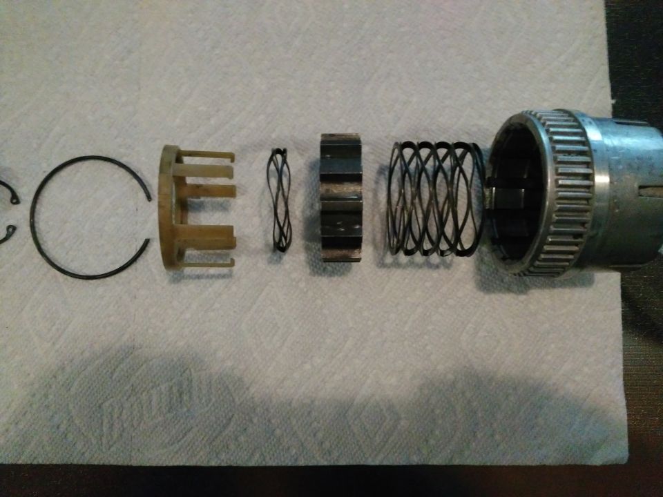 Disassembled transmission one-way clutch parts on paper towel: snap rings, plastic cage, springs, and splined drum