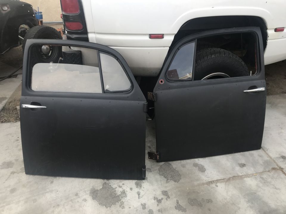 Two black doors from a classic VW Beetle, one on the left, one on the right, leaning against a white pickup truck