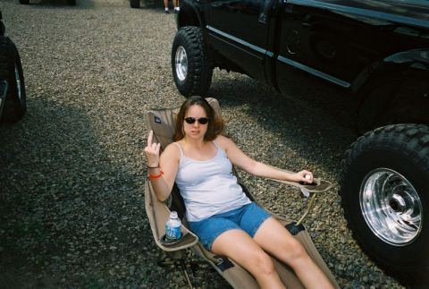 1994 Ford F-150 - A woman sits in a camping chair next to a large black truck, offering a rude gesture.