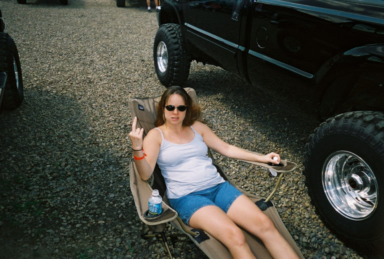 Woman in chair next to lifted black truck, giving the finger