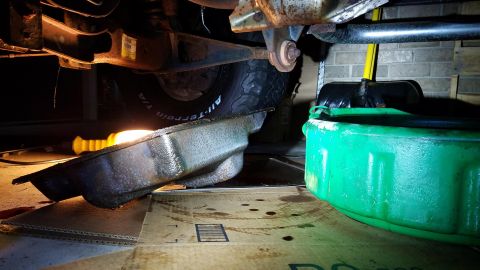 1994 Ford Bronco - Draining oil from a vehicle, with the oil pan and a drain pan positioned underneath.