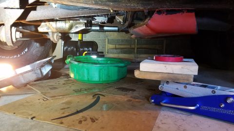 1994 Ford Bronco - The underside of a vehicle is shown with tools and equipment for maintenance, including a drain pan and jack.