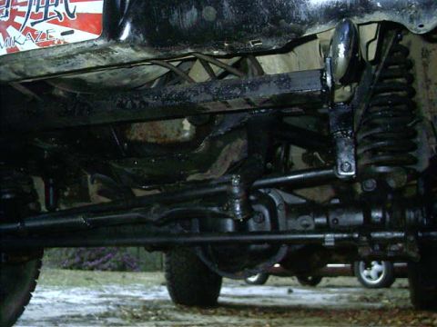 1985 Ford Bronco - The photo shows the underside of a vehicle, focusing on the suspension and steering systems. A second vehicle is partially visible in the b…