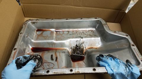 1994 Ford Bronco - A transmission pan shows signs of wear and fluid contamination, with debris being handled by gloved hands.