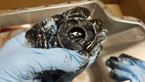 1994 Ford Bronco - A gloved hand holds a dirty transmission filter over an oil pan, indicating the need for maintenance.