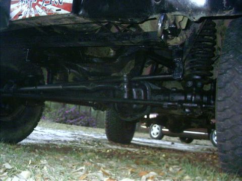 1985 Ford Bronco - The undercarriage of a 1985 Ford Bronco reveals its robust suspension and drivetrain, with another vehicle visible behind it.