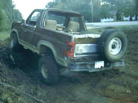 1985 Ford Bronco - This 1980s Ford Bronco is parked on a dirt embankment with trees in the background.