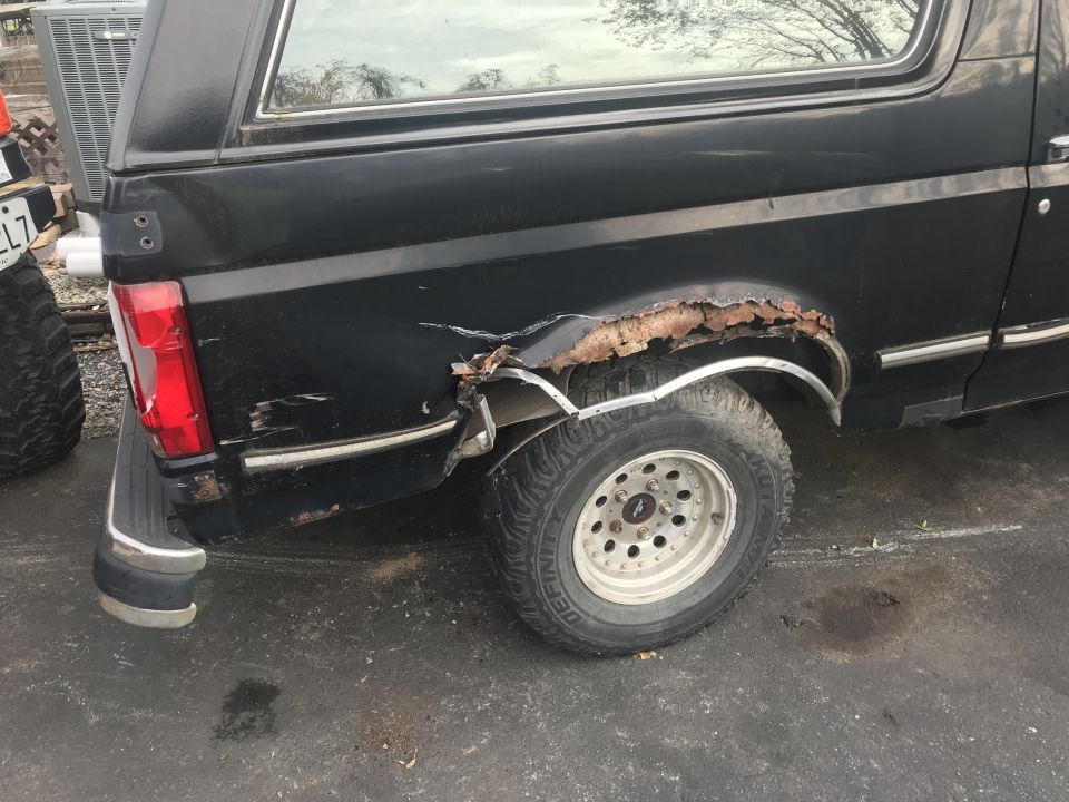 Heavily rusted rear wheel well and quarter panel of a black Ford Bronco.