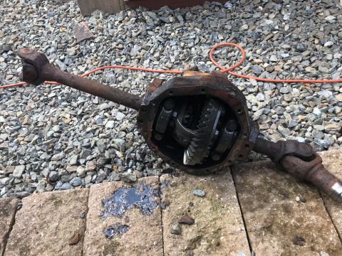 1992 Ford Bronco - A rusty differential assembly with two driveshafts is shown resting on stone pavers with gravel in the background. The differential cover i…
