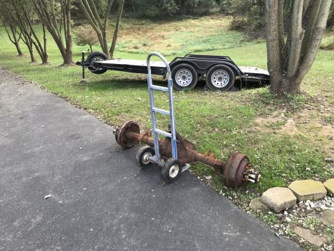 1992 Ford Bronco - A rusty trailer axle with brake drums is mounted on a hand truck in front of a utility trailer parked on grass.