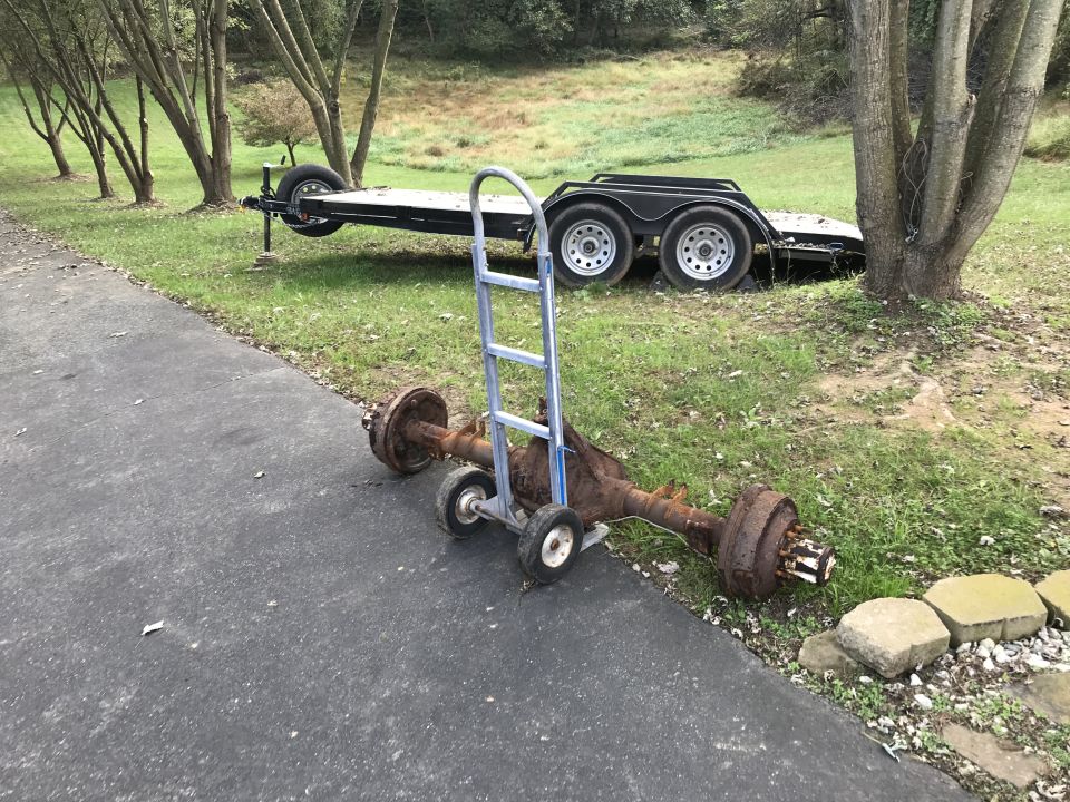 Trailer axle on hand truck in front of a utility trailer.