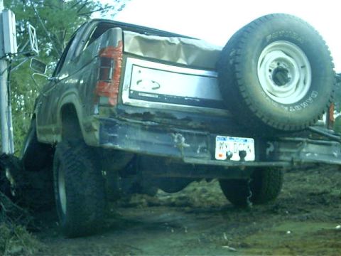 1985 Ford Bronco - The rear of a weathered Ford Bronco, showing its spare tire and a damaged bumper.