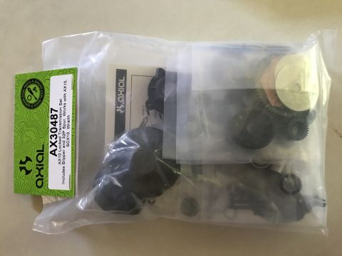 1989 Ford Bronco - A clear plastic bag contains an Axial AX30487 Locked Transmission Set, including gears and other small parts. A green label with the Axial…