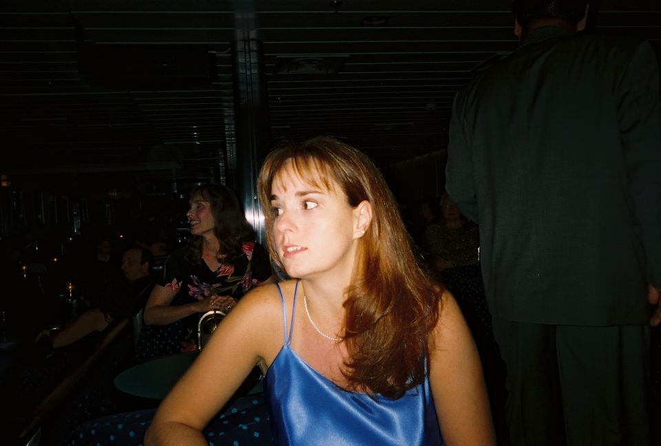 Woman in a blue dress looks to the side, with other people in the background