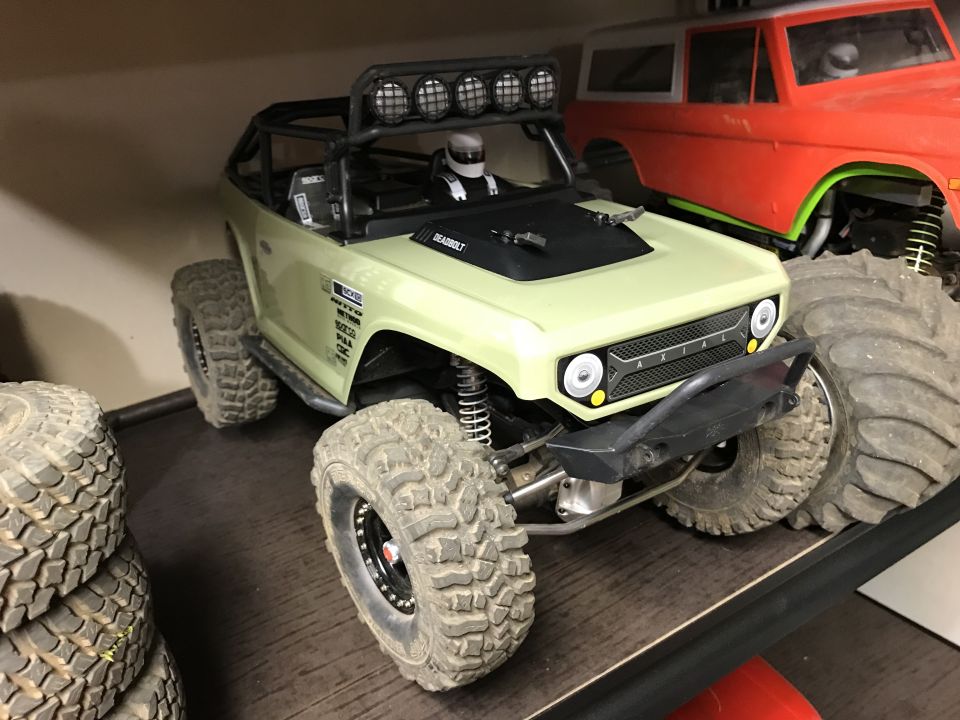 Light green RC rock crawler with large tires next to a red Ford Bronco body.