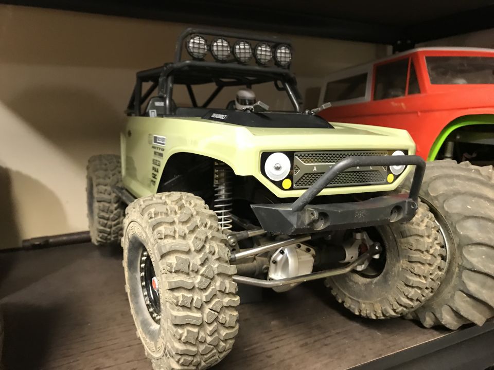 Light green RC rock crawler with large tires and a roll cage, parked next to a red RC vehicle.
