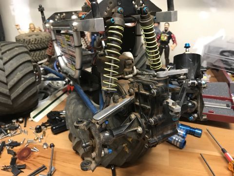 1989 Ford Bronco - Close-up view of the suspension and drivetrain of a remote-controlled monster truck, with various parts and tools scattered on a wooden sur…