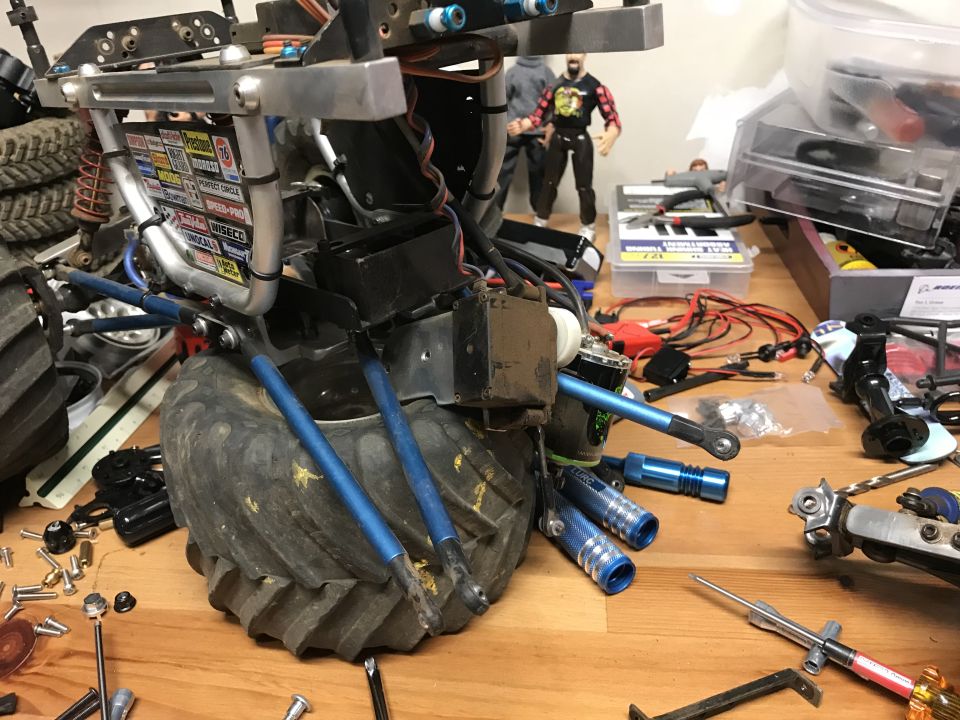 RC monster truck chassis with large tires and blue suspension parts on a workbench with tools.